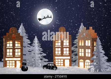 Winterdorf aus Papier. Papier Winter Stadt Nacht Landschaft mit Santa-Klausel Schlitten über Vollmond. Kreative Weihnachtskomposition mit Papierho Stockfoto