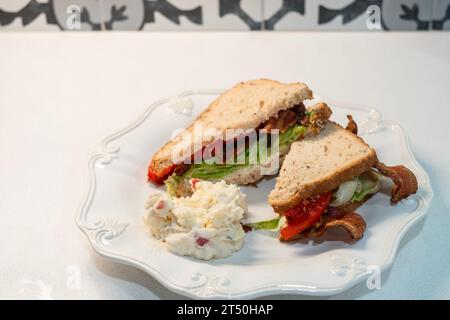 BLT, ein Sandwich mit Speck, Tomaten und Salat aus Haferbrot, mit einer Portion Kartoffelsalat auf einem weißen Teller. USA. Stockfoto