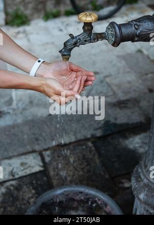 Eine Frau wäscht sich die Hände unter einem alten Wasserhahn auf der Straße. Der alte Teil der Stadt Stockfoto