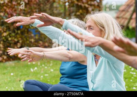 Ältere Frauen werden in einem Moment der Ruhe gefangen, dehnen ihre Hände und üben Yoga in einer ruhigen Gartenumgebung. Ihr Fokus und ihr Engagement Stockfoto