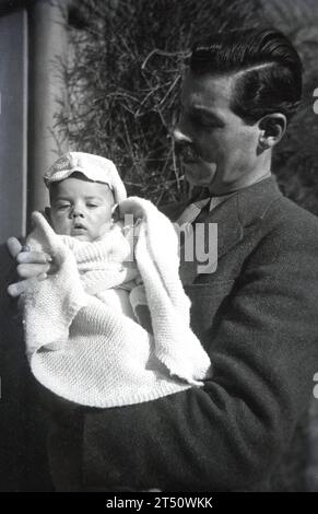 1940er Jahre, historisch, ein Vater stand draußen und hielt seinen Jungen in einen Wollschal gewickelt. Stockfoto