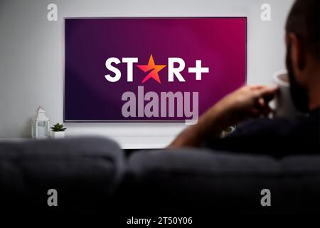 Star Plus auf Smart TV. Mann mit einem Becher und Fernsehen mit einem Star+ Logo auf dem Bildschirm. ROSARIO, ARGENTINIEN - 2. NOVEMBER 2023. Stockfoto