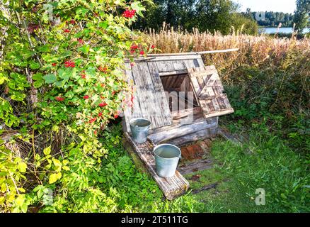 Alter Holzbrunnen auf dem Land mit offener Tür und zwei Metalleimern Stockfoto