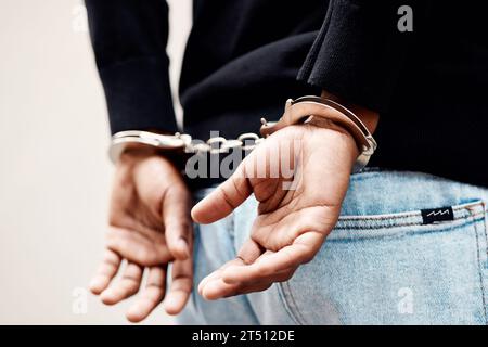 Zurück, Verhaftung und Handschellen mit einem Mann, der verdächtigt wird, von der Polizei aus Nahaufnahme auf grauem Hintergrund. Sicherheit, Gefängnis oder Gefängnis mit einem Mann Stockfoto