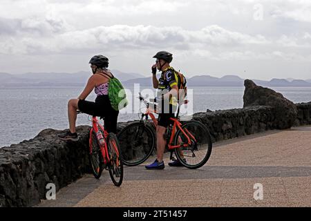 Radspaare machen eine Pause, um die Aussicht auf dem Küstenweg von Las Coloradas nach Playa Blanca auf Lanzarote zu bewundern. Vom März 2023 Stockfoto