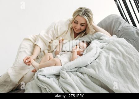 Ein kleines Mädchen liegt im Bett in ihren Händen mit Keksen, einem Schnuller im Mund, geht ins Bett. Die Mutter liegt neben ihrer Tochter. Stockfoto