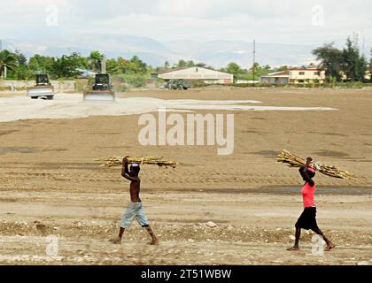 1002199643W-340 PORT-AU-PRINCE, Haiti (19. Februar 2010) Haitianische Kinder transportieren Zuckerrohr über ein Feld, als Seeleute des Amphibious Construction Battalion (ACB) 2 Land für eine Baustelle freilegen. Die ACB-2 führt im Rahmen der Operation Unified Response nach einem Erdbeben der Stärke 7,0 schwere Schäden in und um Port-au-Prince, Haiti, 12. Januar, durch die Bau-, humanitäre und Katastrophenhilfe durch. Marineblau Stockfoto