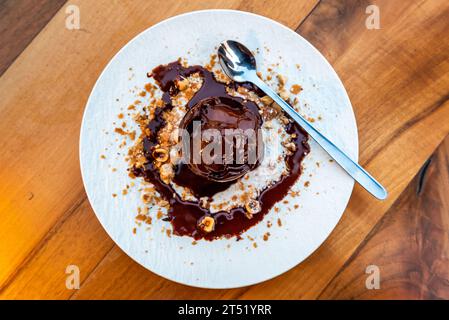 Köstliche Eiskugel auf Teller aus nächster Nähe mit geschmolzenem Schokoladendressing und Haselnüssen auf einem rustikalen Holztisch Stockfoto