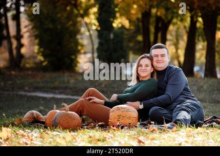 Das liebende Paar sitzt und umarmt auf Karo im Park mit Kürbissen dekoriert, am herbstlichen warmen Tag. Positivität und romantische Männer und Frauen, die T feiern Stockfoto