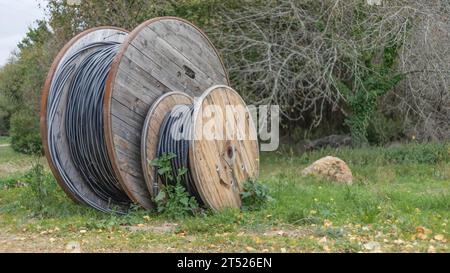 Große Holzspulen mit Rohrleitungen auf dem Gras am Straßenrand Stockfoto