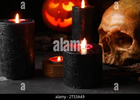 Komposition mit brennenden Kerzen und Schädel für Halloween-Feier auf schwarzem Hintergrund, Nahaufnahme Stockfoto