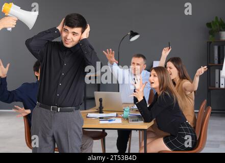 Junger Geschäftsmann, der unter lauten Kollegen im Büro leidet Stockfoto