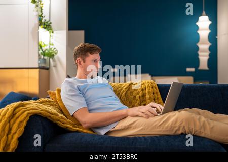 Seriöser Mann, ein freiberuflicher Mitarbeiter, der im Dunkeln zu Hause an einem Laptop arbeitet und den Bildschirm betrachtet. Stockfoto