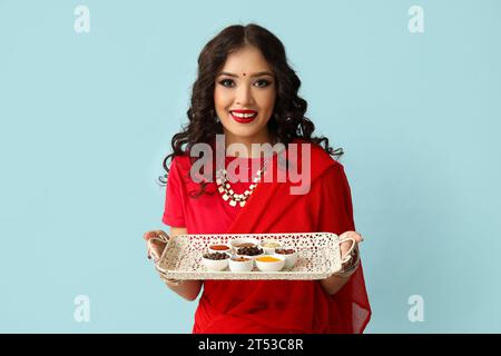 Schöne indische Frau im Sari, die Tablett mit verschiedenen Gewürzen auf blauem Hintergrund hält Stockfoto