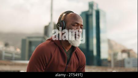 Mann, Kopfhörer und müde von Bewegung, Stadt und Herausforderung in Outdoor-Fitness, Ermüdung und dehydriert. Schwarze reife Person, erschöpft und trainiere dich Stockfoto