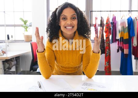 Glückliche, birassische Modedesignerin, die Videoanrufe am Schreibtisch im Studio hat Stockfoto