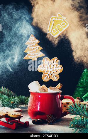 Rote Tasse mit Marshmallows und Zimt und fliegenden Weihnachts-Lebkuchenkeksen in einer Wolke aus Mehl und Kakao. Festliches Essen. Stockfoto