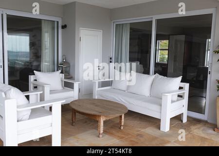 Leeres großes graues Wohnzimmer mit weißer Couch, Stühlen, Kissen und großen Fenstern Stockfoto