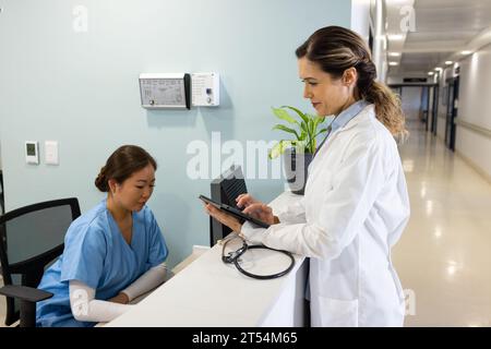 Diverse Ärztinnen mit Tablet und Computer arbeiten an der Rezeption des Krankenhauses Stockfoto