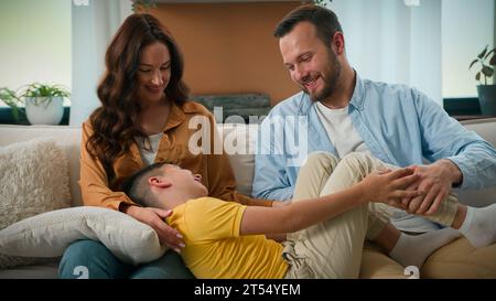 Glückliche kaukasische Familie Vater Mutter mit süßem Kind Sohn kitzeln Spaß haben Entspannen Sie sich auf dem Sofa zusammen sorglose Eltern Kind Junge lachen spielen Kuscheln zu Hause Stockfoto