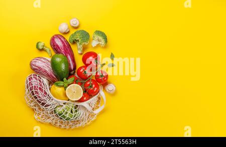 Netzbeutel gefüllt mit verschiedenen Gemüsesorten. Flach über gelbem Hintergrund mit Kopierraum Stockfoto