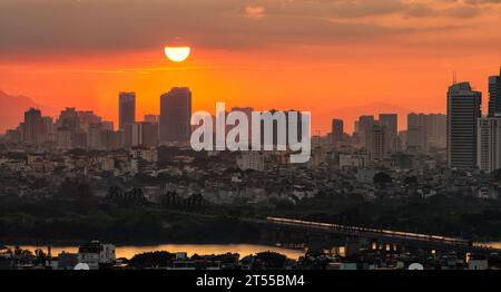 Ein Zug kommt zum Endbahnhof, auf der Long Bien Brücke, über den Roten Fluss, unter gelbem Sonnenuntergang, Hanoi, Vietnam Stockfoto