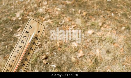 Holzthermometer mit roter Messflüssigkeit, das hohe Temperaturen über 36 Grad Celsius an sonnigem Tag auf trockenem Rasen anzeigt. Wärmekonzept Stockfoto