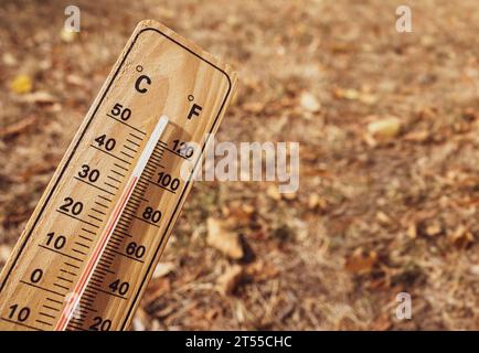 Holzthermometer mit roter Messflüssigkeit, das hohe Temperaturen über 36 Grad Celsius an sonnigem Tag auf trockenem Rasen anzeigt. Wärmekonzept Stockfoto