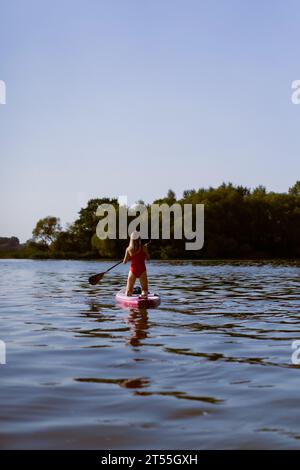 Frau in rotem Badeanzug paddelt im Sommer auf dem See. Supboard Stockfoto