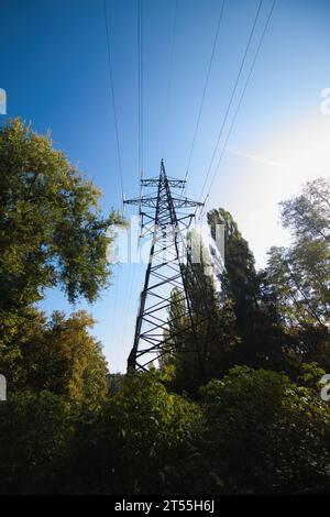 Großer eiserner Turm von Stromleitungen in grünem Bereich unter blauem Himmel Stockfoto