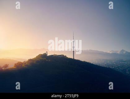 Luftdrohnenaufnahme von Symbol Almaty City hoher Fernsehturm und Park auf dem Koktobe Hügel vor Schnee Berge bei Sonnenaufgang in Kasachstan Stockfoto