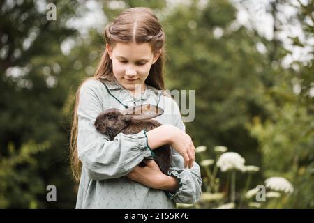 Ein Mädchen, das ein Vintage-Kleid trägt, hält ein Kaninchen Stockfoto