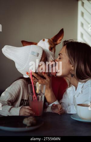 Mom und Tochter im Café mit Hund. Mamas Kuss. Tierfreundlich. Stockfoto