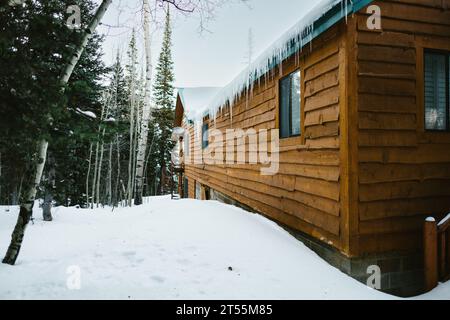Eiszapfen auf der Rückseite einer Blockhütte im Winter mit schneebedecktem Boden Stockfoto