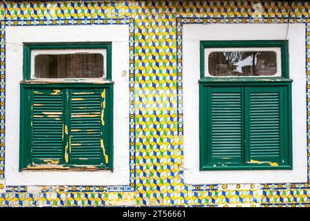 Zwei verwitterte Fenster über der gefliesten verglasten Fassade. Belem Viertel, Lisboa, Portugal Stockfoto