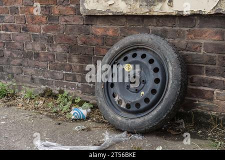 London, England, 17. Juli 2023. Ein entsorgter schwarzer Autoreifen liegt an einer verwitterten Ziegelwand. Der Reifen weist sichtbaren Verschleiß und Schmutz auf. Stockfoto