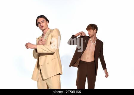 Hübscher junger Mann im beigefarbenen Anzug posiert mit einem anderen männlichen Model in einem nicht geknöpften Anzug, Männer Power Stockfoto