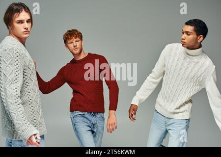 Drei gutaussehende multiethnische männliche Models in lässigen, gemütlichen Pullover, die sich in Bewegung posieren, Männer Power Stockfoto
