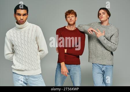 Junges multiethnisches Trio mit lässigen Pullis und Jeans posiert und in die Kamera schaut, Männer Power Stockfoto
