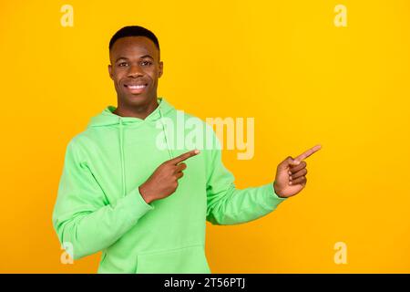 Porträt der guten Stimmung optimistischer Hipster tragen stilvoller Pullover, der auf dem Verkauf leere Fläche auf hellgelbem Hintergrund anzeigt Stockfoto