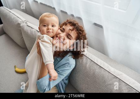 Eine überglückte Frau mit geschlossenen Augen, die die niedliche Tochter eines Kleinkindes auf der Couch im Wohnzimmer hält Stockfoto