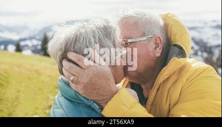 Glückliches Seniorenpaar mit zärtlichen Momenten während des Wandertages in den Bergen - Winter- und Liebeskonzept - weicher Fokus auf das Ohr des Mannes Stockfoto