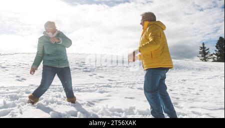 Glückliches Seniorenpaar, das sich während des Schneeballschlages im Freien amüsiert - Konzept für Winter und aktive ältere Menschen - weicher Fokus auf das Männergesicht Stockfoto