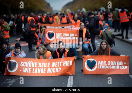 Letzte Generation Blockade DEU, Deutschland, Deutschland, Berlin, 28.10.2023 Demonstranten der Initiative Letzte Generation Extinction Rebellion XR und Fridays for Future mit Transparent Schoene Heile Welt hier wie lange Noch und Artikel Art 20A GG Grundgesetz Leben schuetzen bei der Blockade der Straße 17. Juni in Berlin Deutschland . Die Gruppe fordert die Bundesregierung auf, drastischere Massnahmen zur Senkung der Treibhausgasemissionen zu ergreifen und bis 2030 die Nutzung aller fossilen Brennstoffe einstellen en: Protesters from the Initiative Last Generation Extinction Rebellion XR and Stockfoto