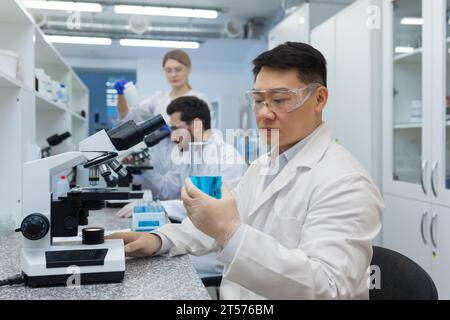 Ernsthaft denkender asiatischer Wissenschaftler, der mit Mikroskop im Labor arbeitet, Mann im weißen medizinischen Mantel Wissenschaftler, der an der Probenforschung arbeitet. Stockfoto