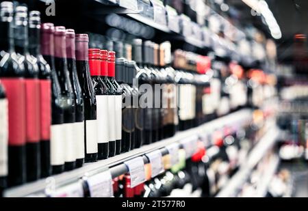 Spirituosengeschäft, Spirituosengeschäft. Rotwein auf dem Regal. Konzentrieren Sie sich auf Flaschen, Supermarktgang im Hintergrund. Verkauf von alkoholischen Getränken und Auswahl im Lebensmittelmarkt. Stockfoto