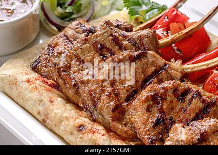 Schweinefleisch, Lammrippen auf Pita-Brot, mit gebackenem Paprika und Sauce, auf einem weißen Teller, auf weißem Hintergrund Stockfoto