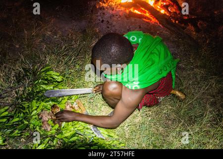 MASAI MARA, KENIA - 20. FEBRUAR 2020: Masai man schneidet ein Ziegenbein, Kenia Stockfoto