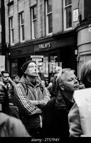 Mann in einer Menge von Demonstranten mit Adidas Jacke und Hut auf dem Pro-Palestine march, Grey Street. Schwarz-weiß. Newcastle upon Tyne, Großbritannien - 28. Oktober 2023 Stockfoto