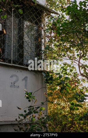 Die Zahl 21 ist mit einer Schablone auf eine graue Balkonwand unter einem Fenster mit Gittern gemalt. Hausnummer 21. Ecke eines umgebenen Gebäudes Stockfoto